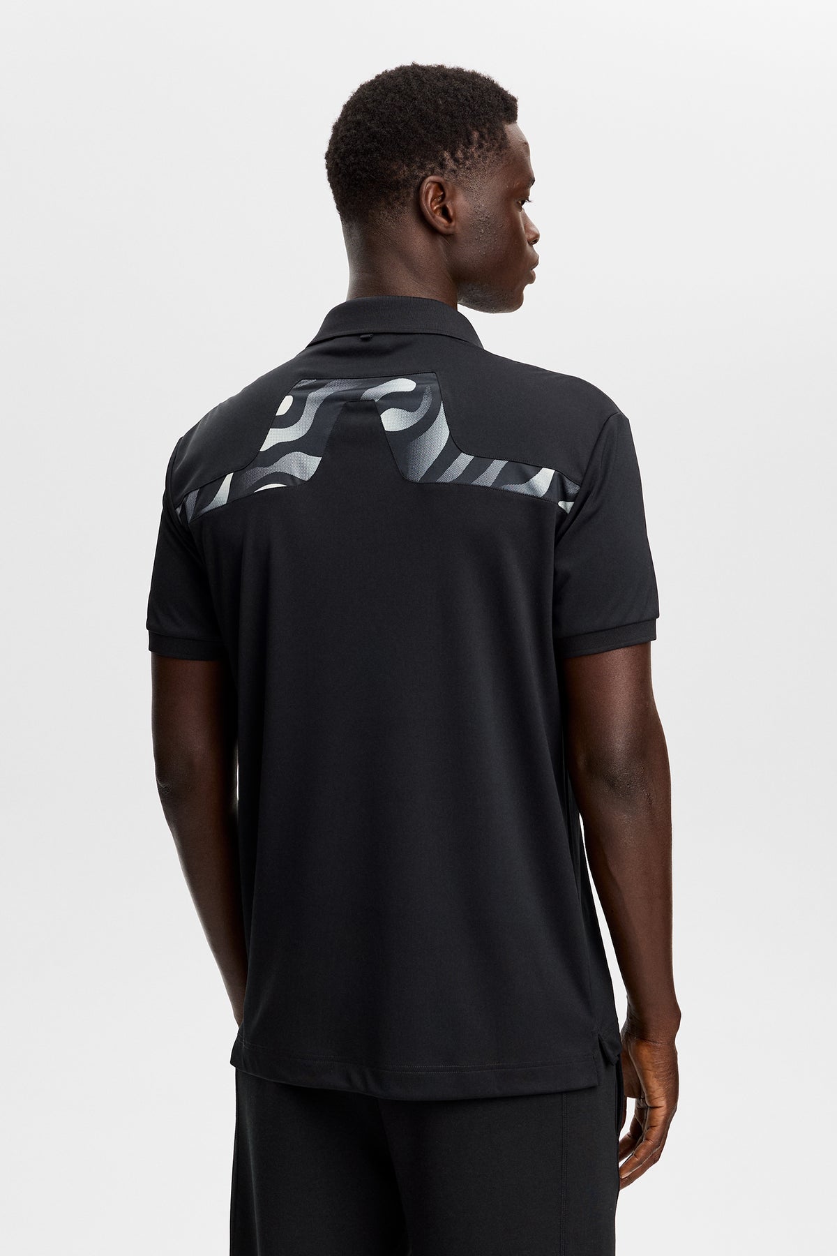 J.Lindeberg KV Print Polo Black – lifestyle on-course shot demonstrating UPF 40+ sun protection